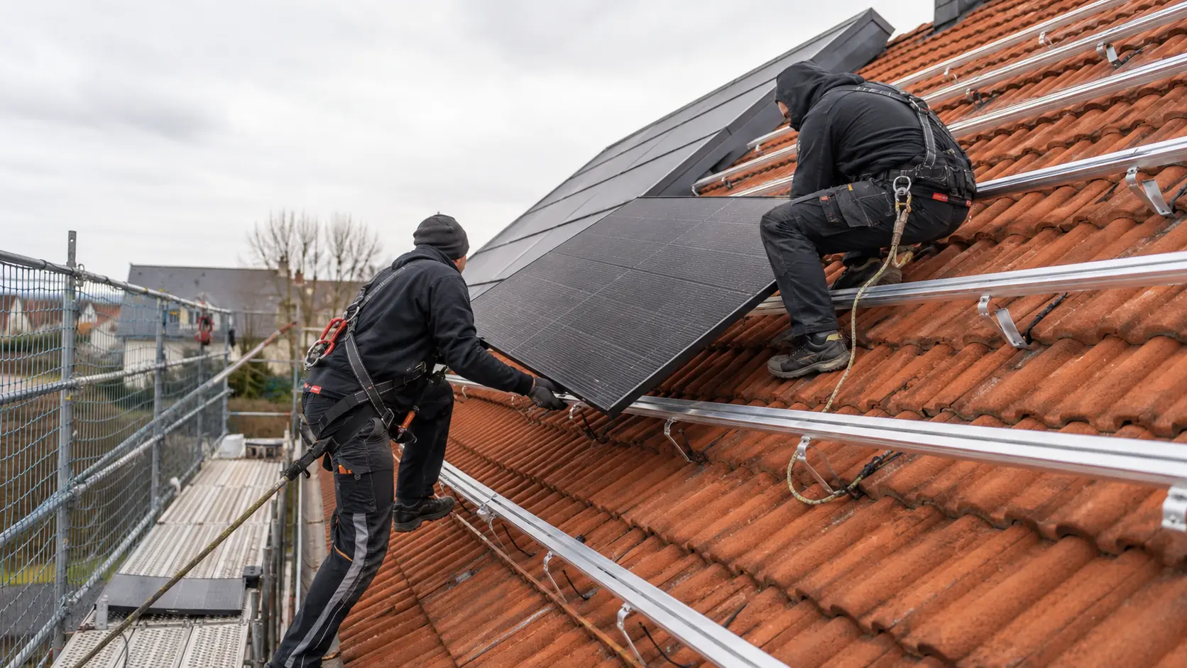 Fachkräfte montieren Photovoltaikmodule auf der Unterkonstruktion eines Ziegeldachs